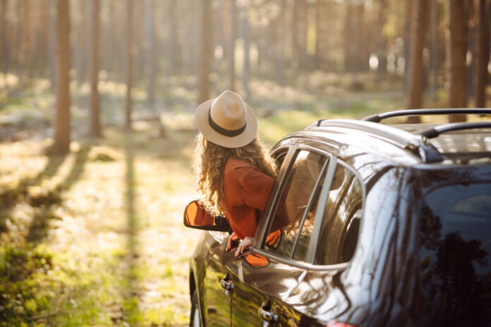 Portrait of a young woman with curly hair enjoying the sunset from the car window.