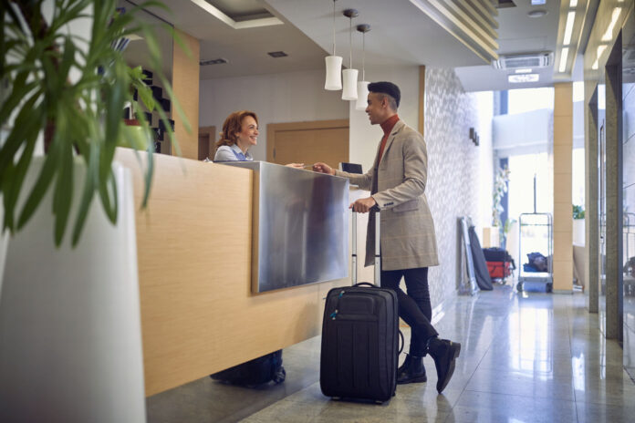 young afro-american male paying with card to a friendly female caucasian at reception desk